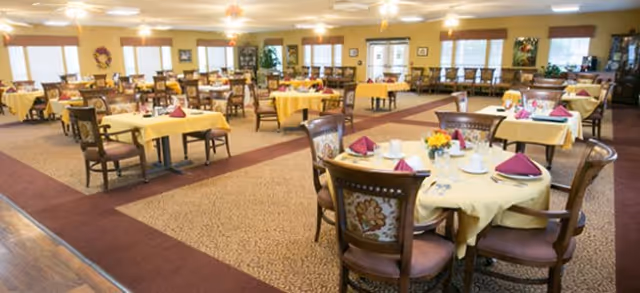 Spacious dining room with round tables draped in yellow tablecloths and wooden chairs set for meals.