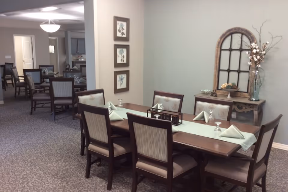 Interior dining room with a long wooden table set with folded napkins and chairs, and a decorative sideboard against a mint-colored wall.