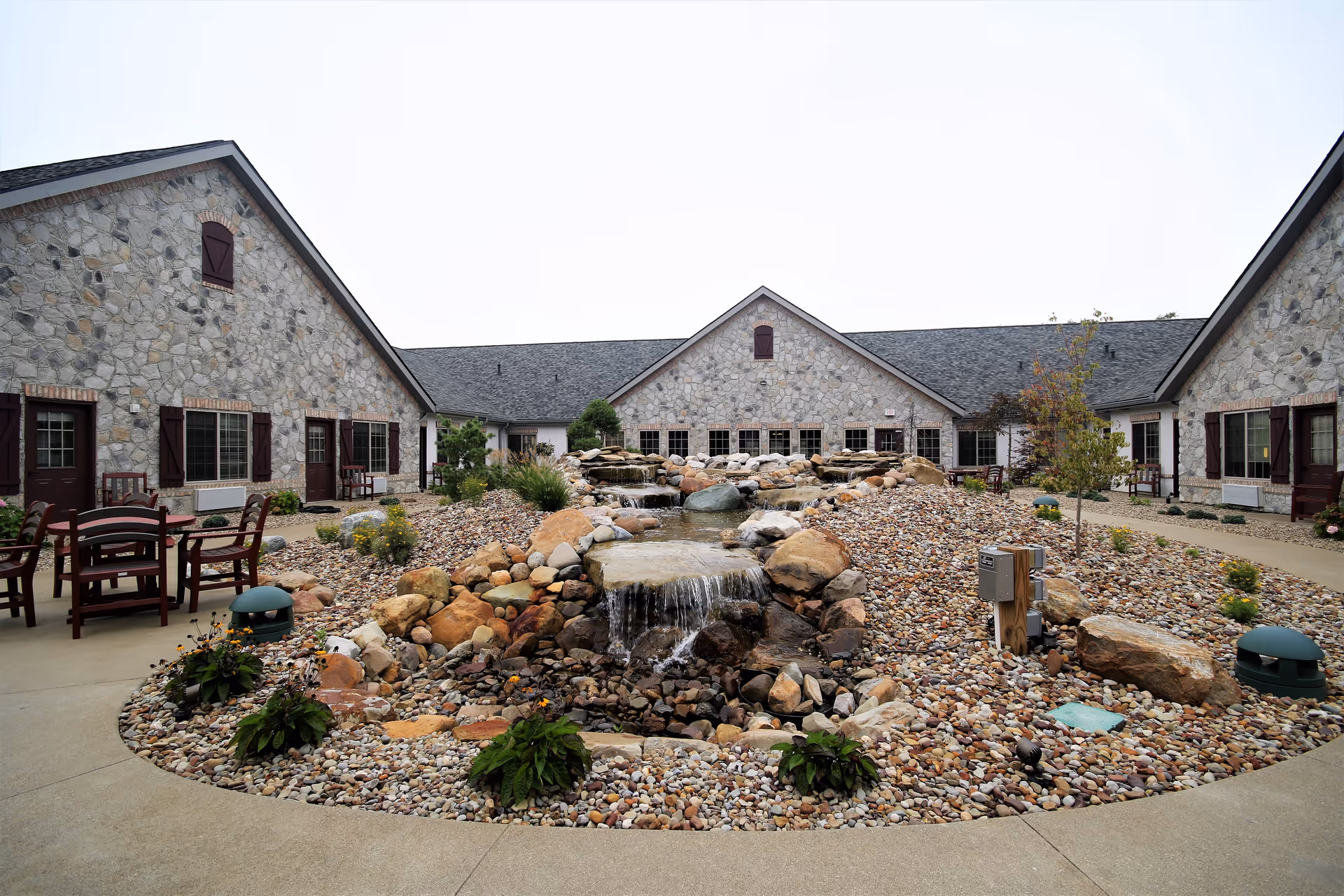 Courtyard with a central rock water feature and seating surrounded by stone-clad single-story buildings.