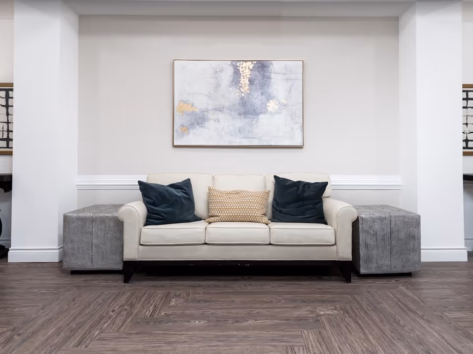 Cream sofa with three pillows centered against a neutral wall under abstract artwork, flanked by two gray cube side tables on wood flooring.