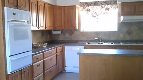 Bright kitchen with oak cabinets, white appliances, a central island, and a window with a floral valance.