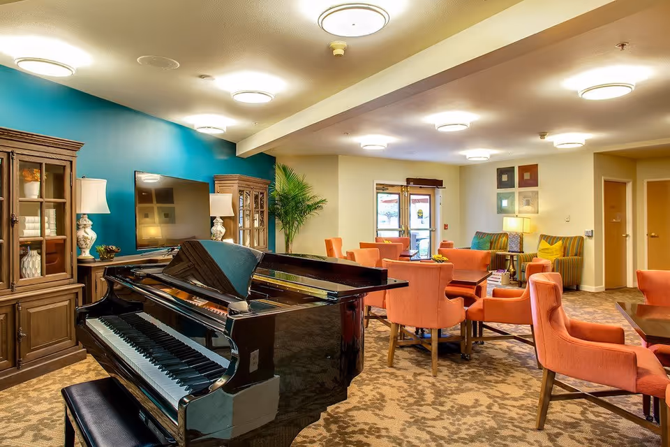 A grand piano in a cozy lounge with orange chairs and teal accent wall.