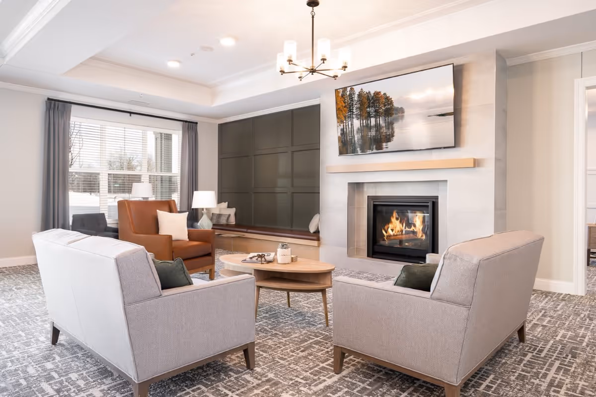A bright common living room with sofas and armchairs arranged around a coffee table and a fireplace with a mounted TV above it.