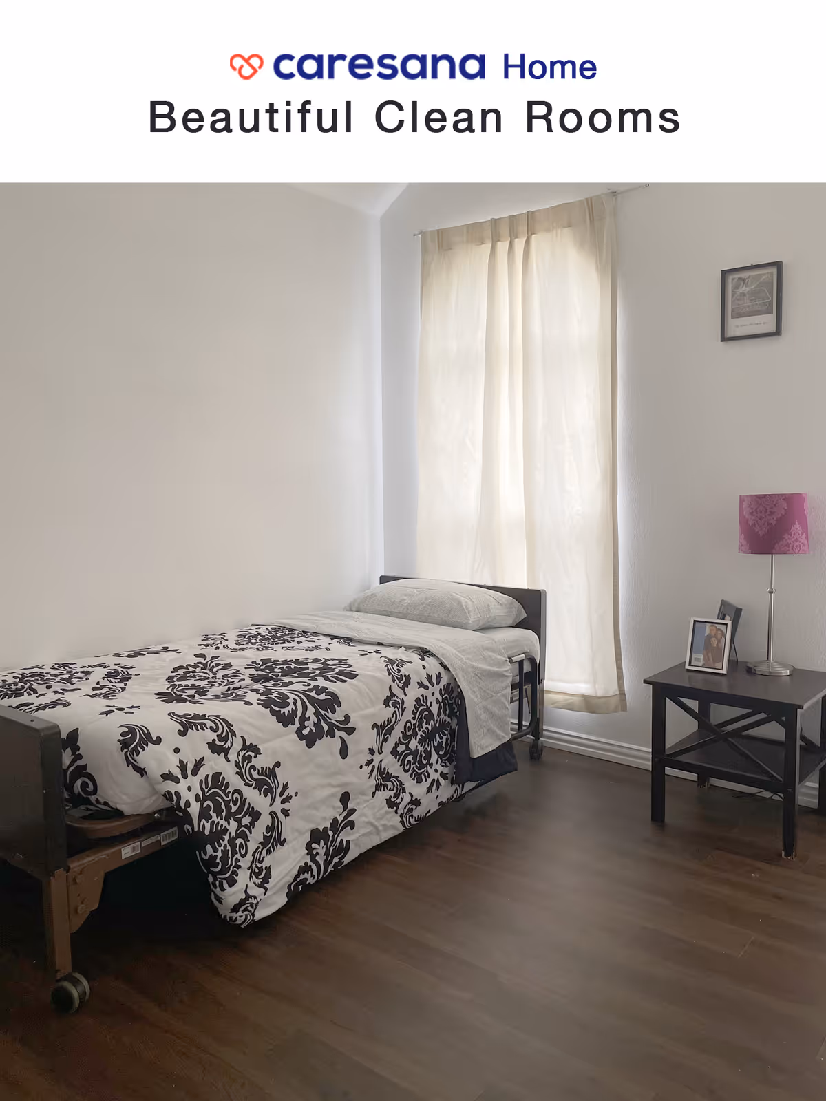 A clean and simple bedroom with a single bed covered in a white and black patterned comforter. The bed is positioned against a white wall with a window covered by light beige curtains. Next to the bed is a black nightstand with a purple lamp and two framed photos. The floor is dark wood.