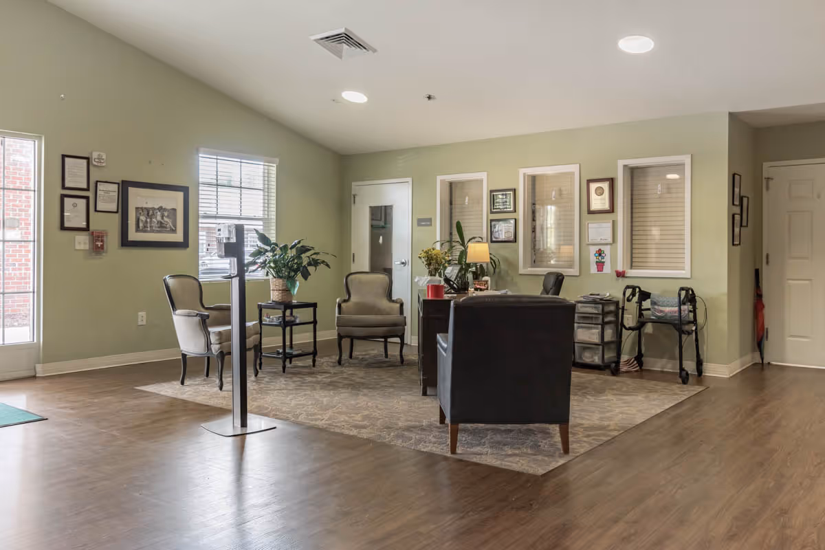 Reception lounge area with seating, a desk, plants, and windows in a senior living facility.