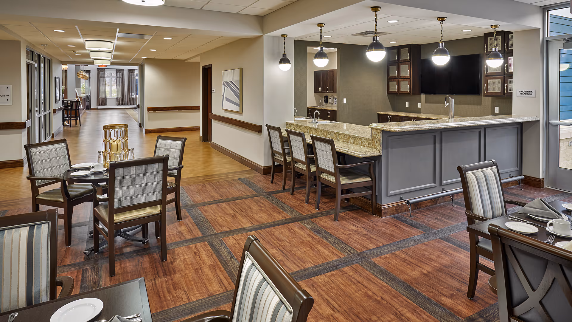 Bright, modern dining room with multiple tables and chairs and a granite-topped service bar with pendant lights.