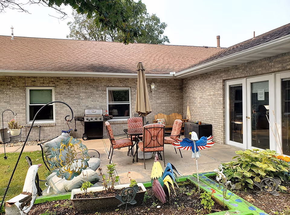 Brick-walled outdoor patio with a dining table and chairs under an umbrella, a grill, and decorative garden ornaments in front.