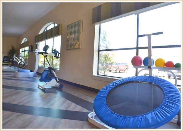 Bright fitness room with a stationary bike, a small trampoline, exercise balls and large windows.