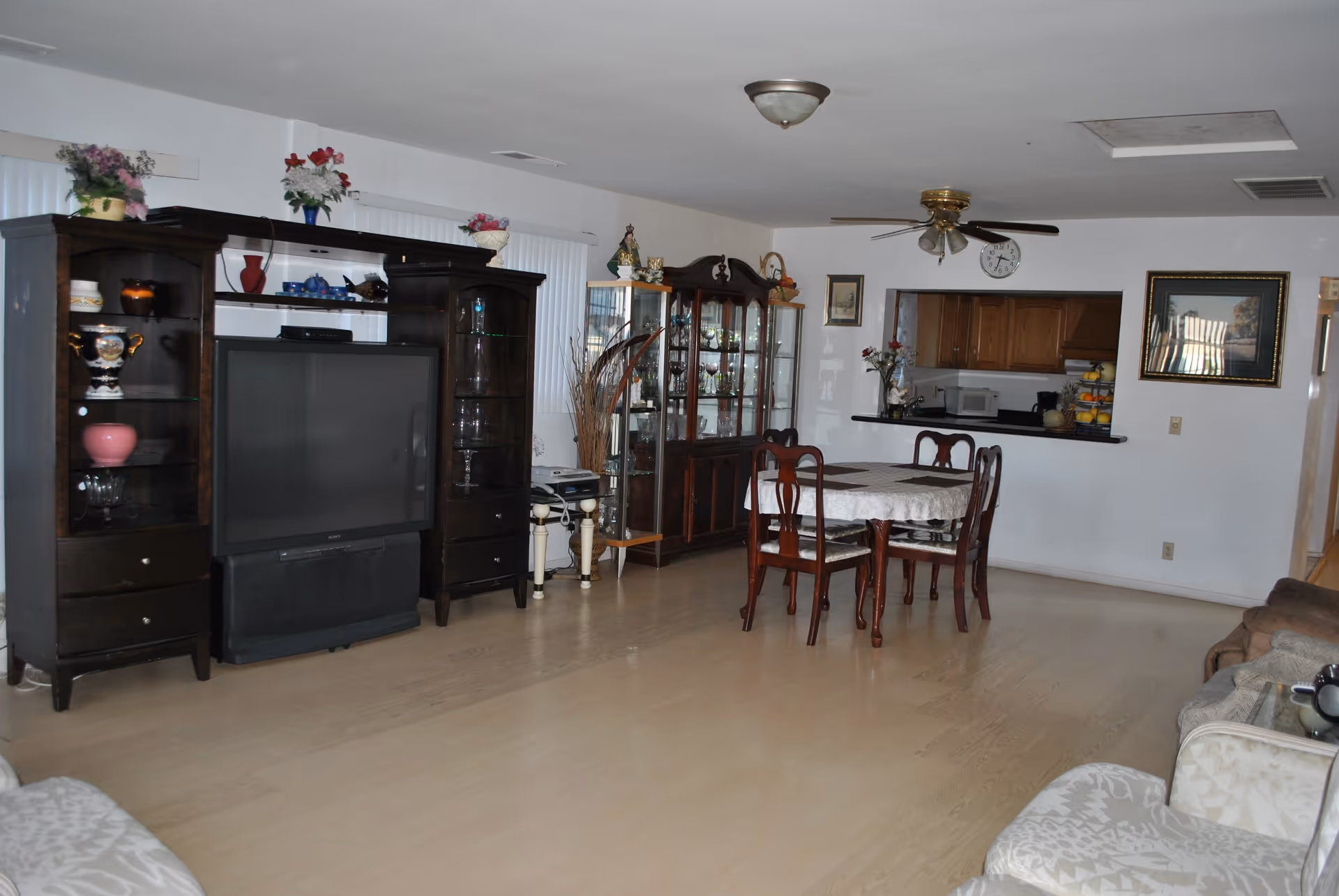 Open living and dining area with a large dark wood entertainment center and TV, a dining table and chairs, a china cabinet, and a pass-through to the kitchen.