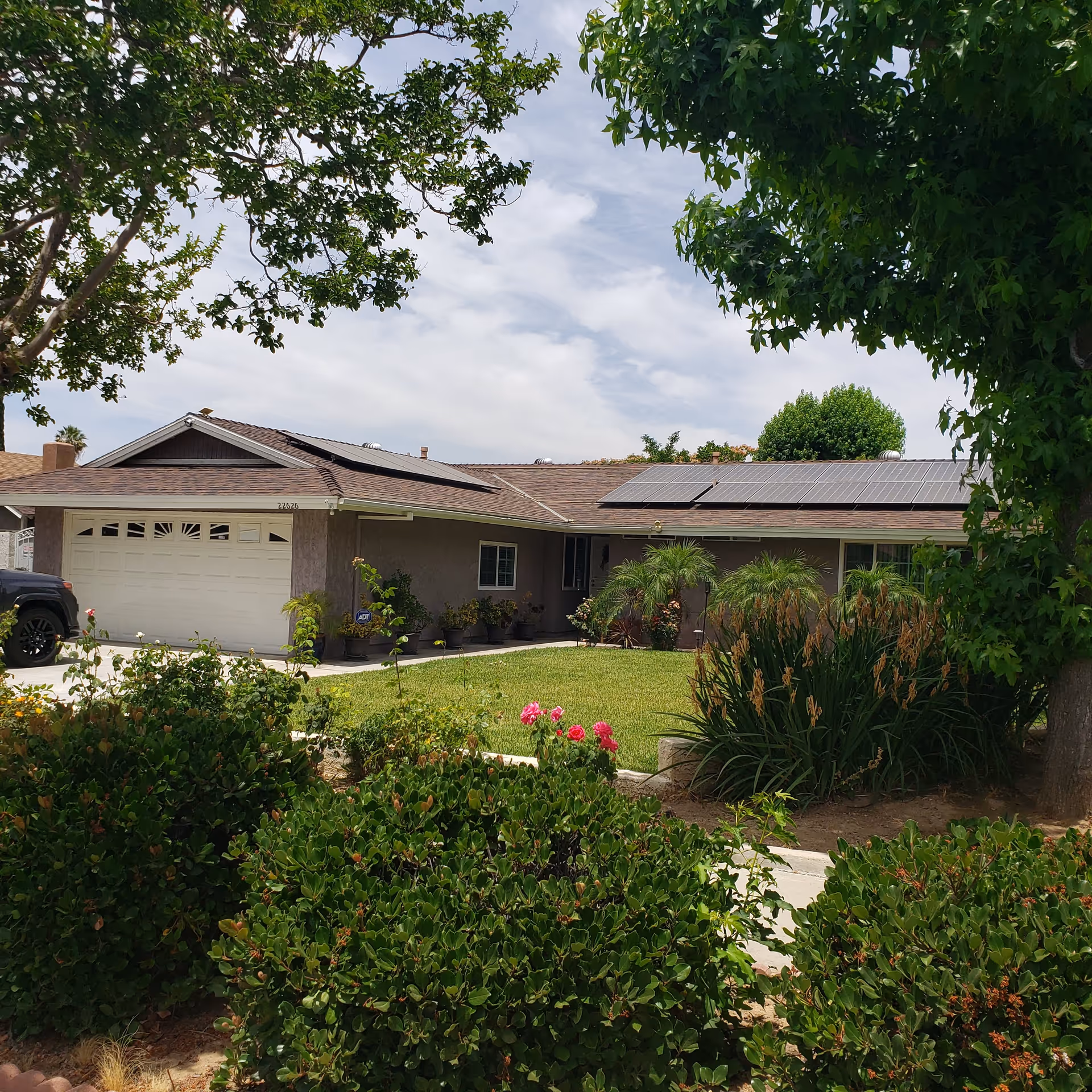 A view of the exterior of Terrace Gardens, showcasing a house with solar panels on the roof, surrounded by green grass and colorful flowers.