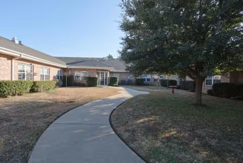 Curved concrete path through a campus lawn toward a brick senior living building.