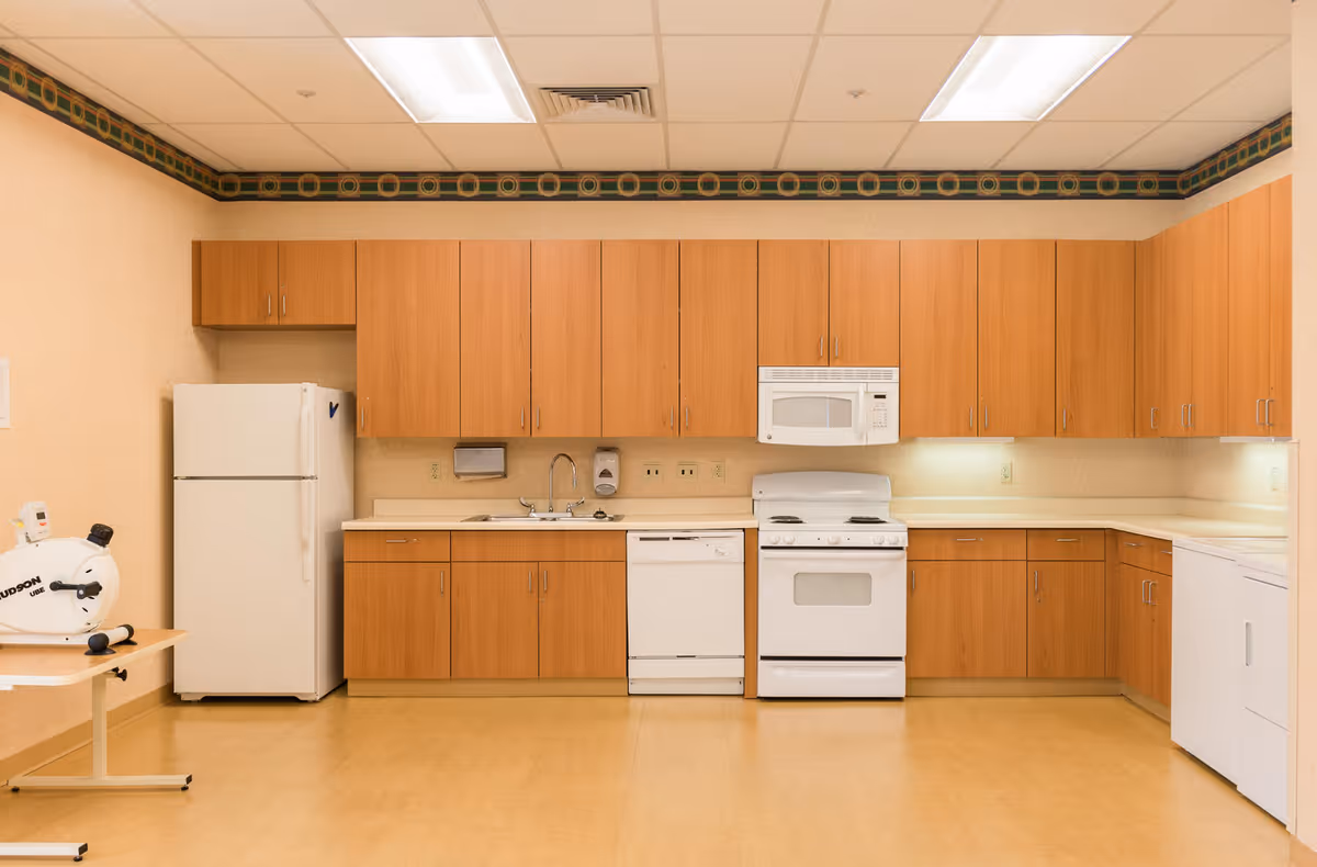 Communal kitchen with wood cabinets, a sink and white appliances including a refrigerator, dishwasher, stove and microwave.