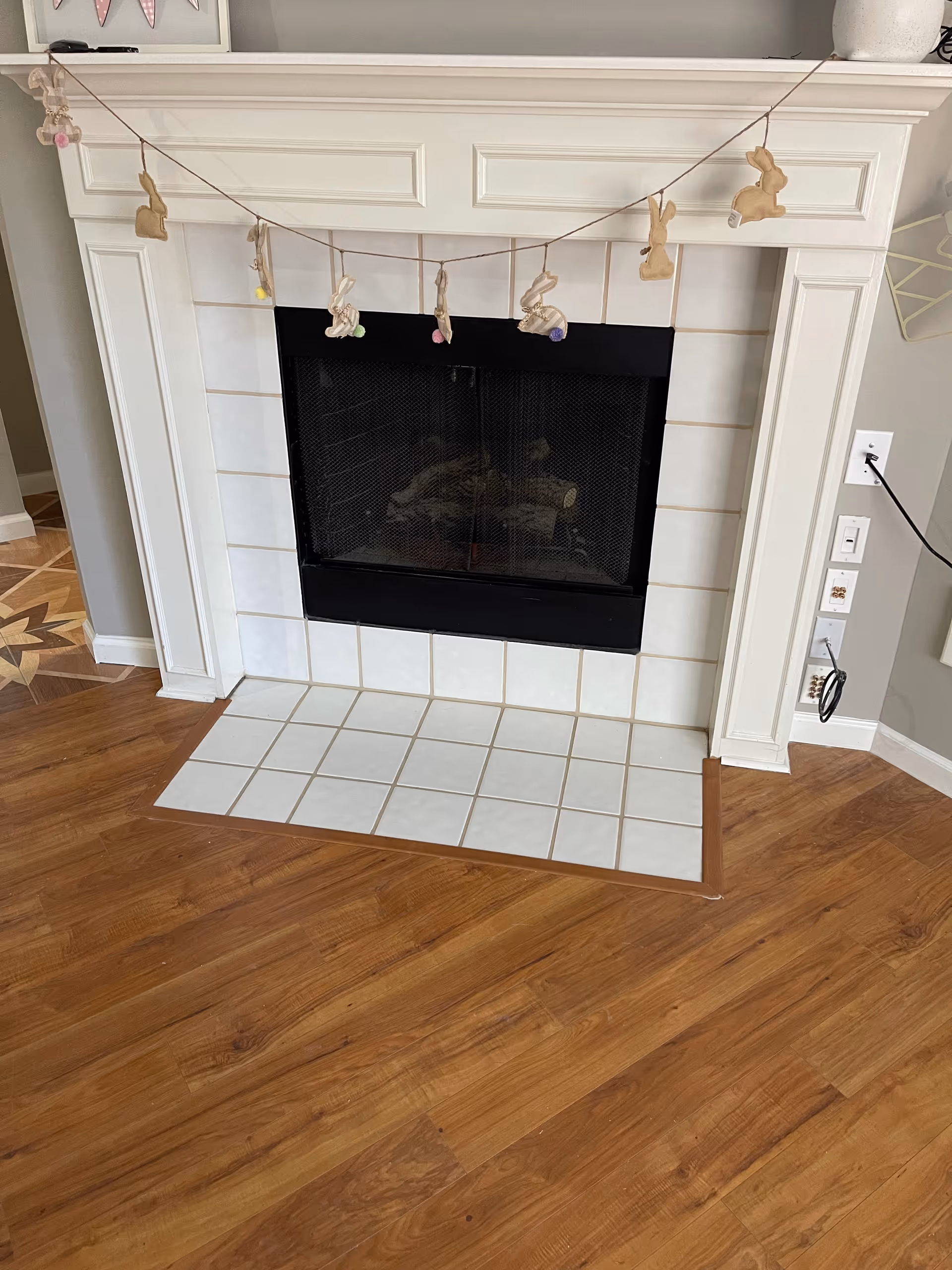 White tiled fireplace with a white mantel decorated with a bunny garland and wood-look flooring