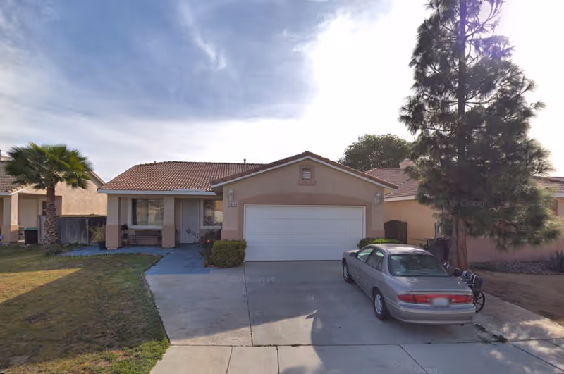 Single-story stucco house with attached two-car garage, driveway with a parked car and front lawn.