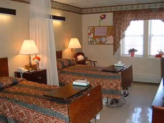 A shared senior living bedroom with two beds, curtains, and a bulletin board