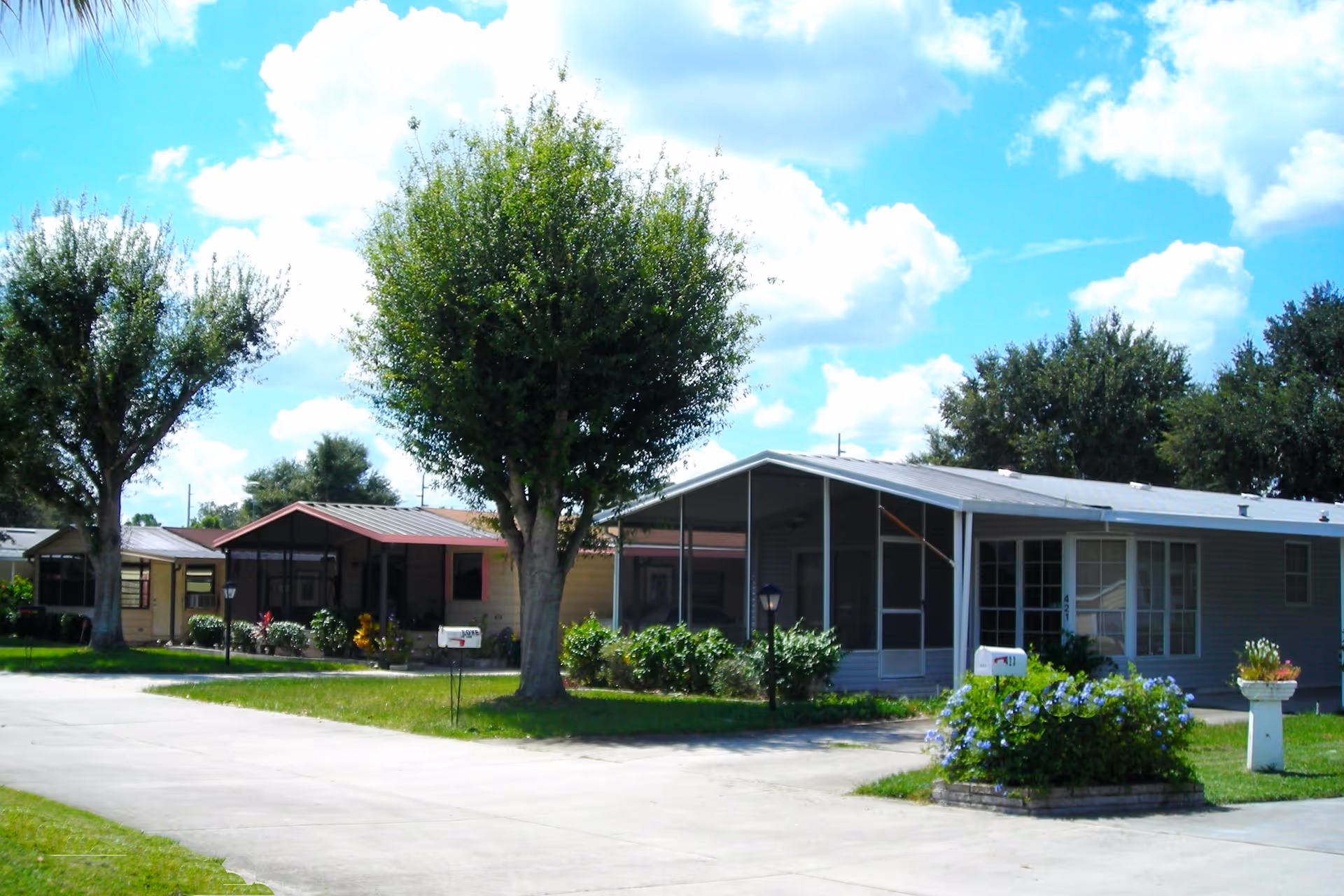 Single-story manufactured homes with screened porches, trees, and driveways in a sunny retirement community.