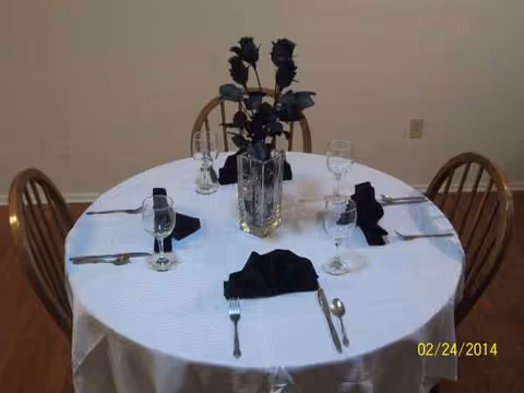 Round dining table set with black napkins and tall flower centerpiece.
