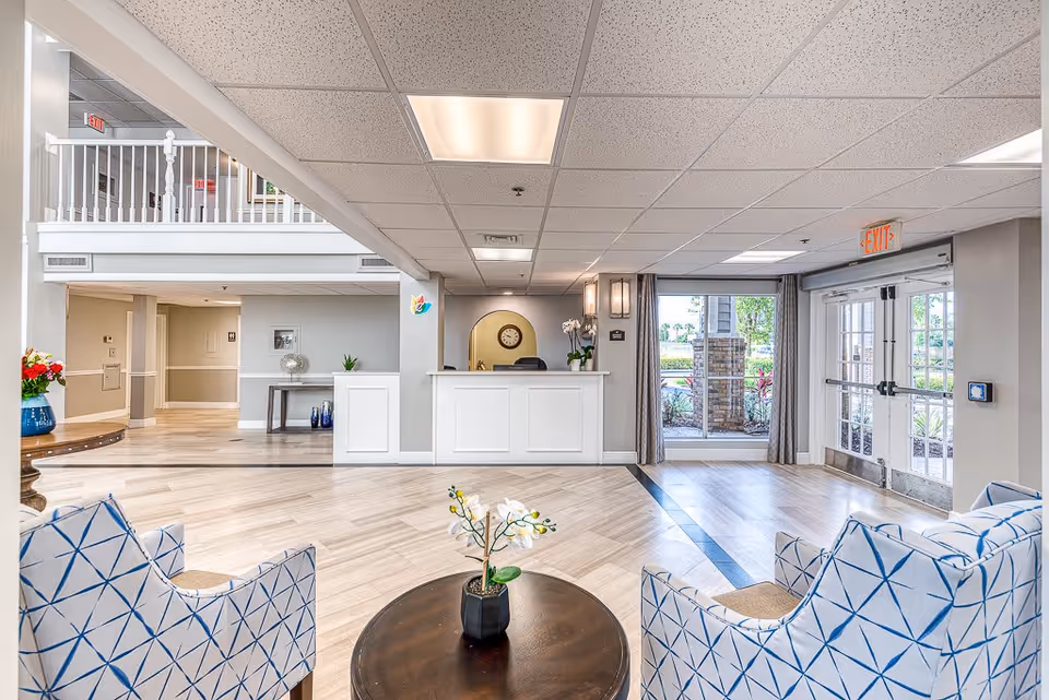 Bright reception lobby with a front desk, seating area, and double glass entrance doors.