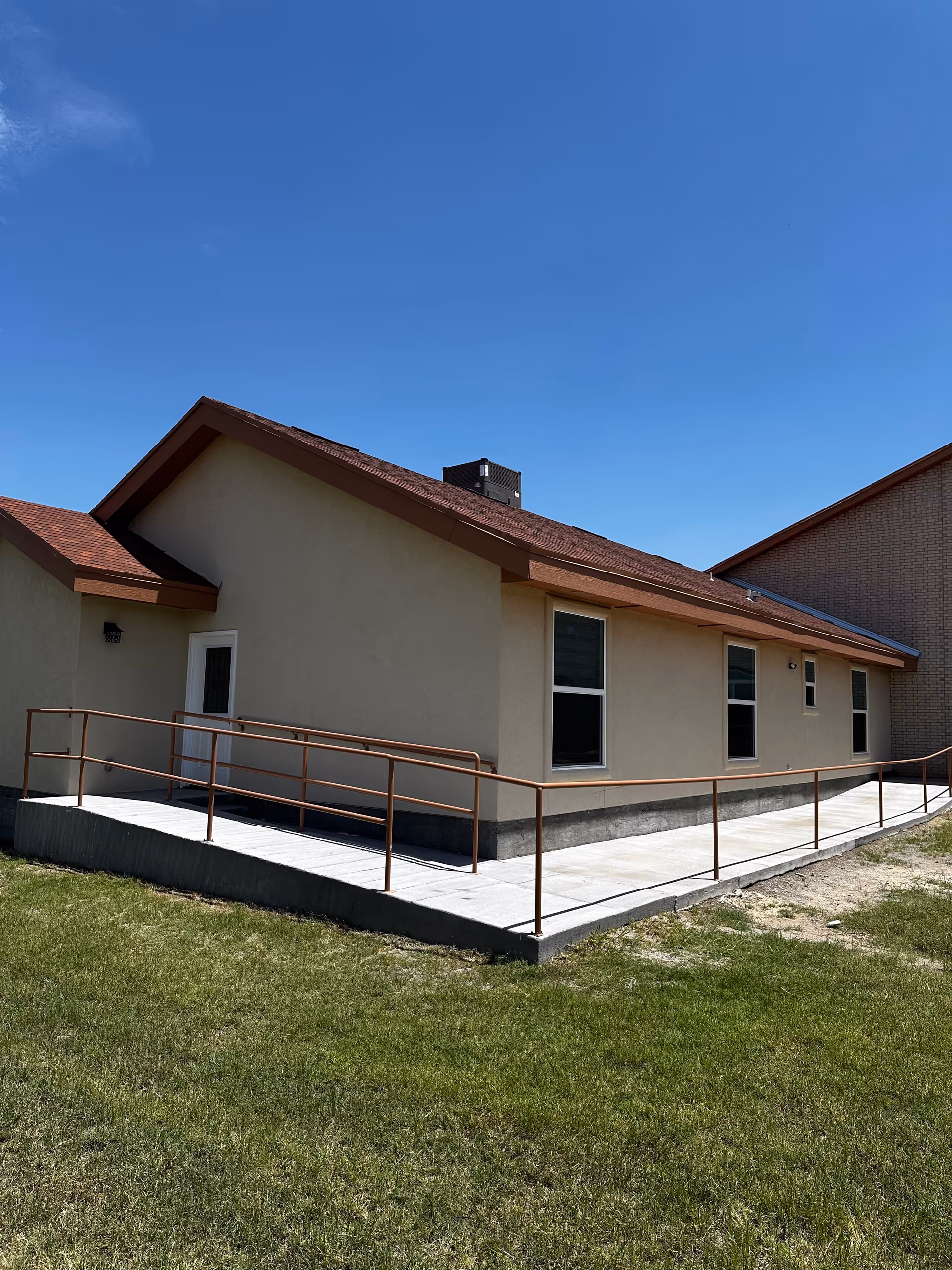 Single-story building with a ramp, green grass, and a clear blue sky in the background.