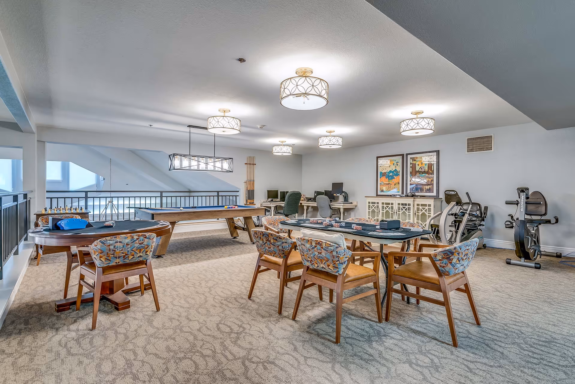Spacious senior community activity room with card tables, a pool table, exercise bikes, and seating under ceiling lights.