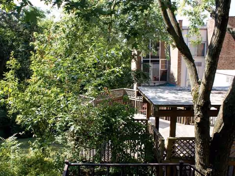 Outdoor wooden deck with lattice railing, surrounded by trees beside a brick building.