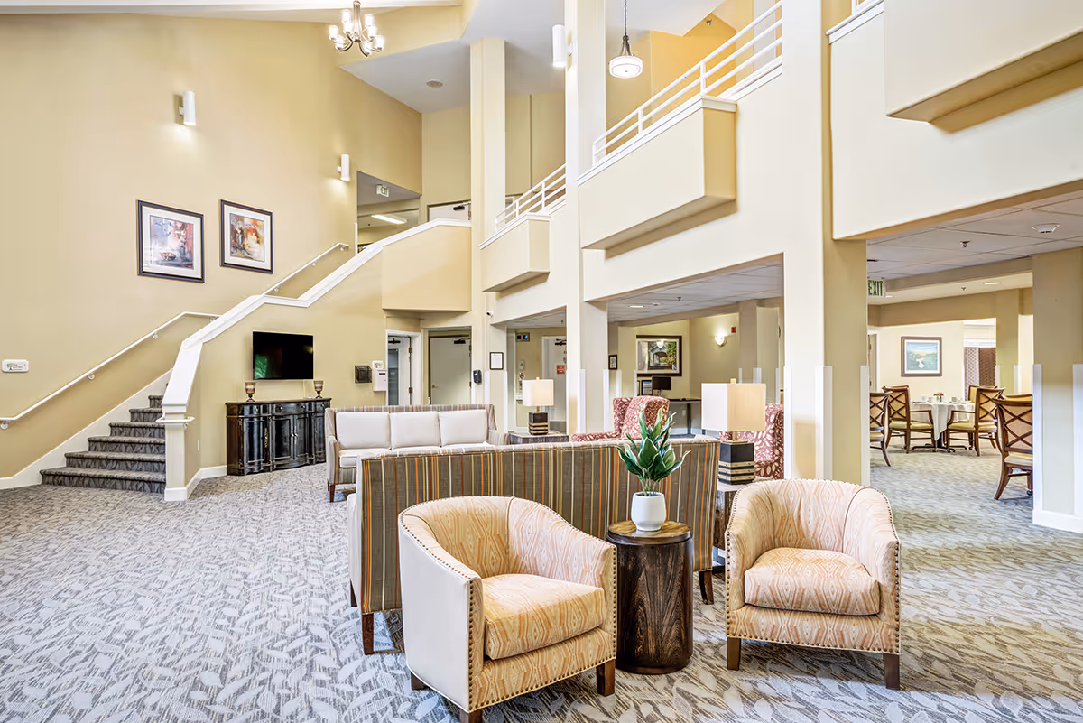 Spacious two-story senior living lobby with seating areas, armchairs, sofas, and a staircase.