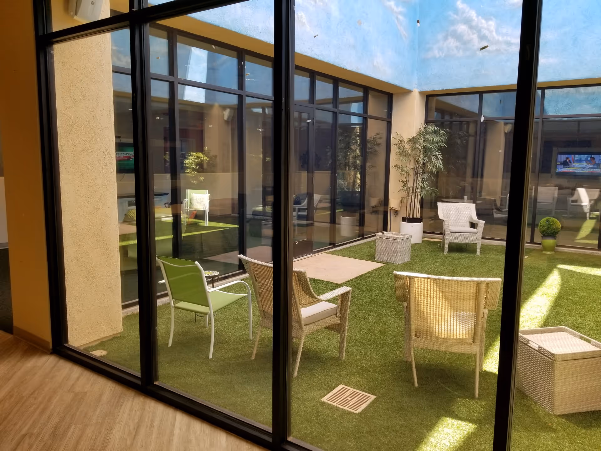 Enclosed indoor courtyard with glass walls, seating chairs, potted plants, and artificial grass.