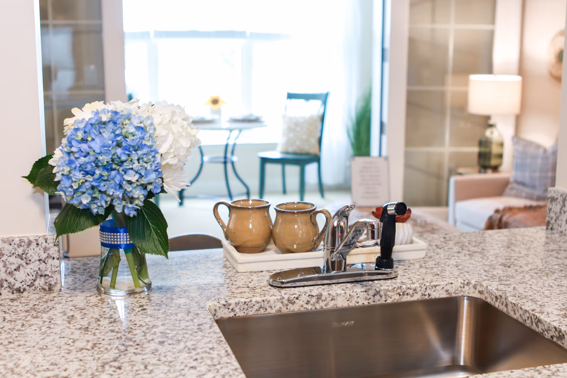 Granite kitchen counter with a sink, mugs, and a blue hydrangea bouquet.