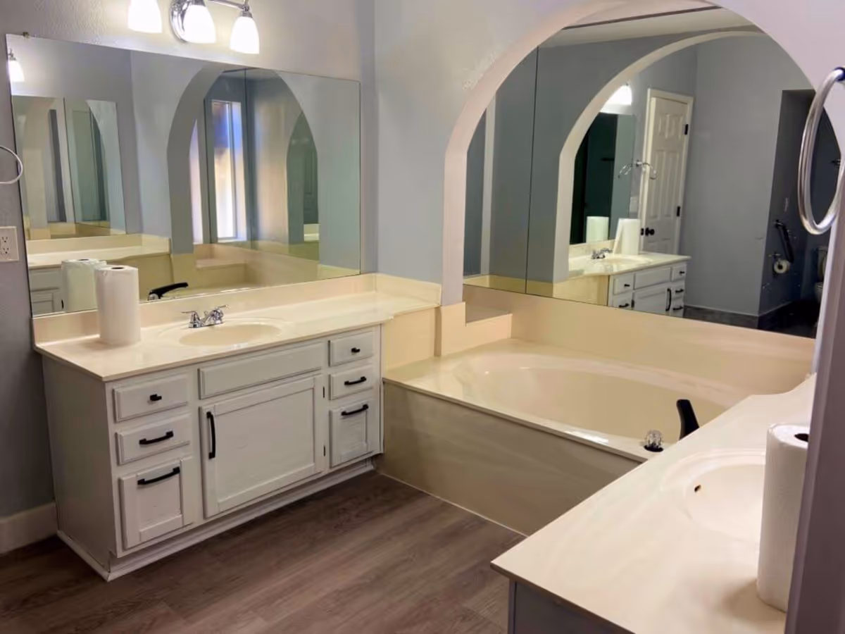 Bathroom with double vanities, a built-in soaking tub, large mirrors, and wood-look flooring.
