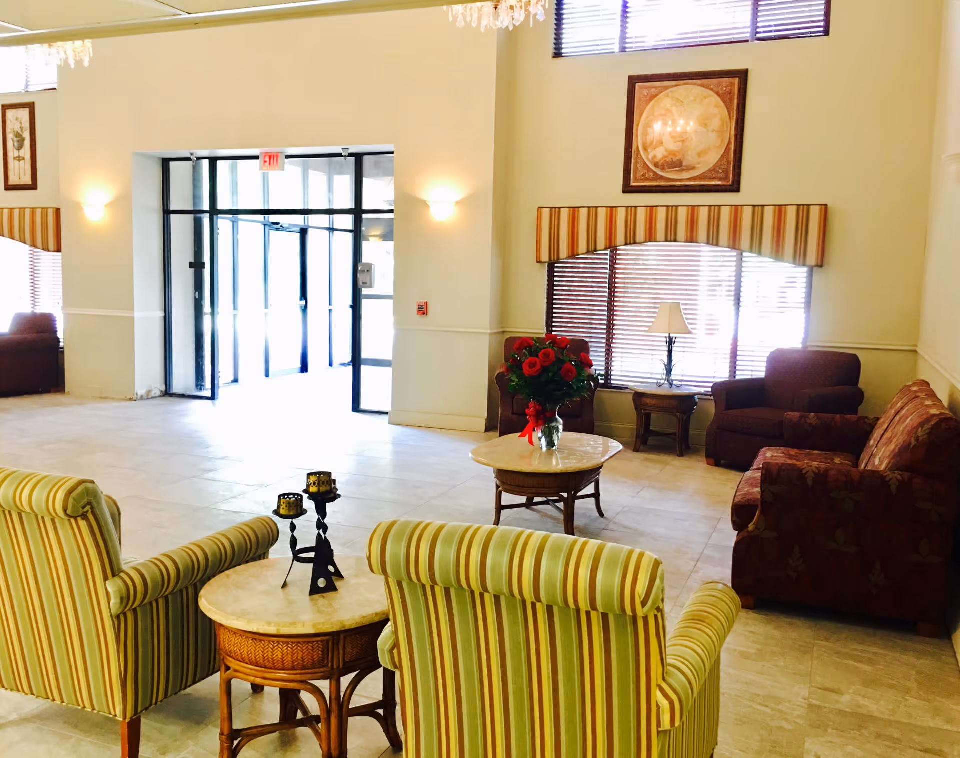 Bright senior living facility lobby with striped armchairs, couches, coffee tables and a glass-door entrance.