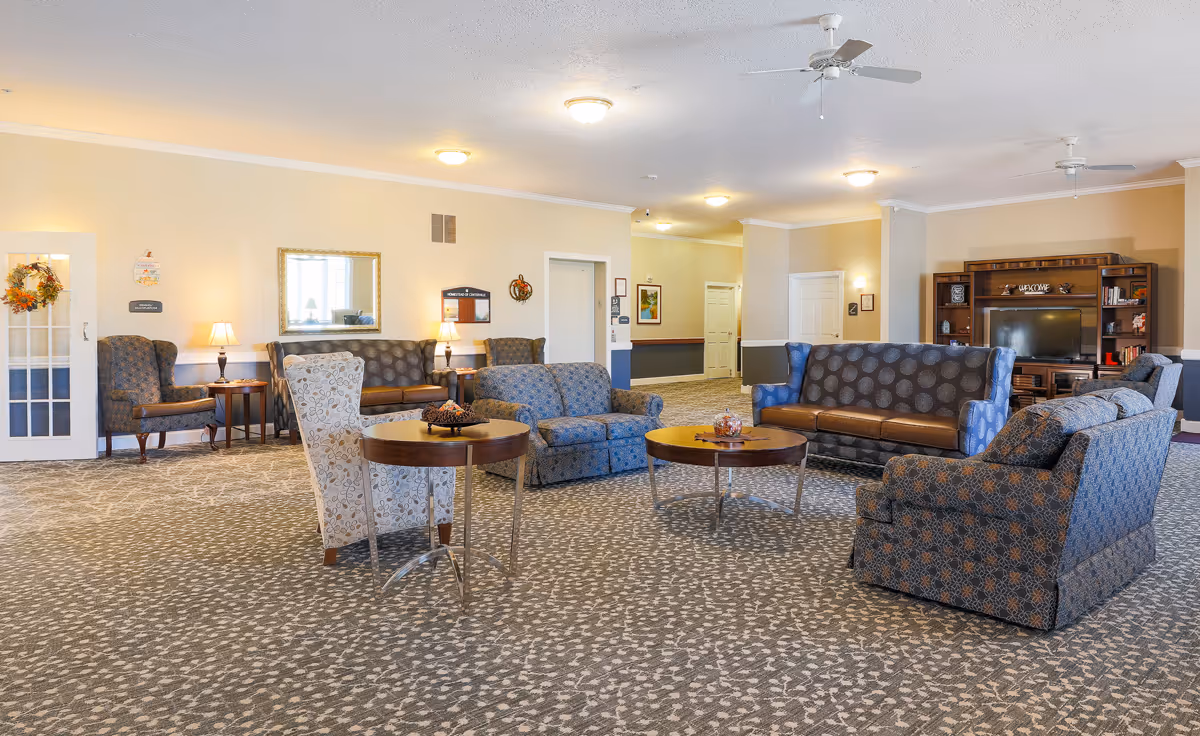 Spacious senior living common area with multiple sofas, armchairs, coffee tables, and a TV entertainment center.