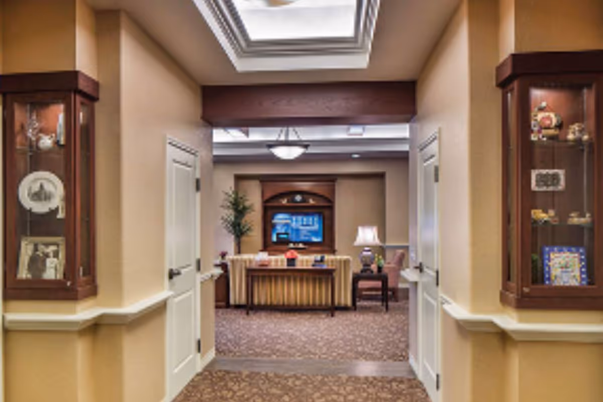 Hallway opening into a cozy communal sitting room with a sofa, television, lamp, and decorative display cabinets.