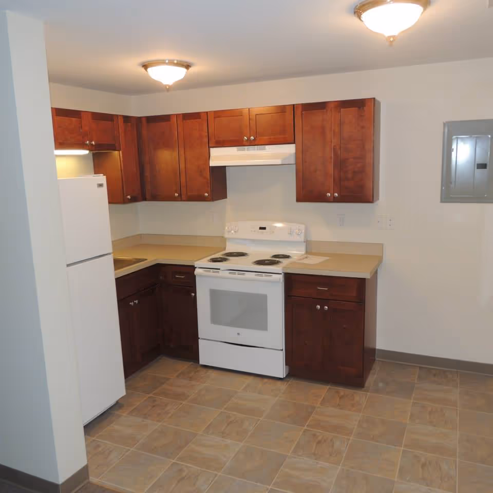 Small kitchen with white refrigerator and stove, wooden cabinets, beige countertops and tiled floor.