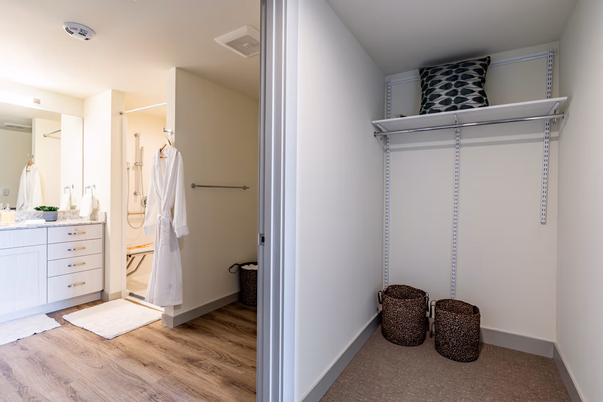 Bright bathroom with a vanity and shower on the left and an adjacent empty closet with shelves and baskets on the right.