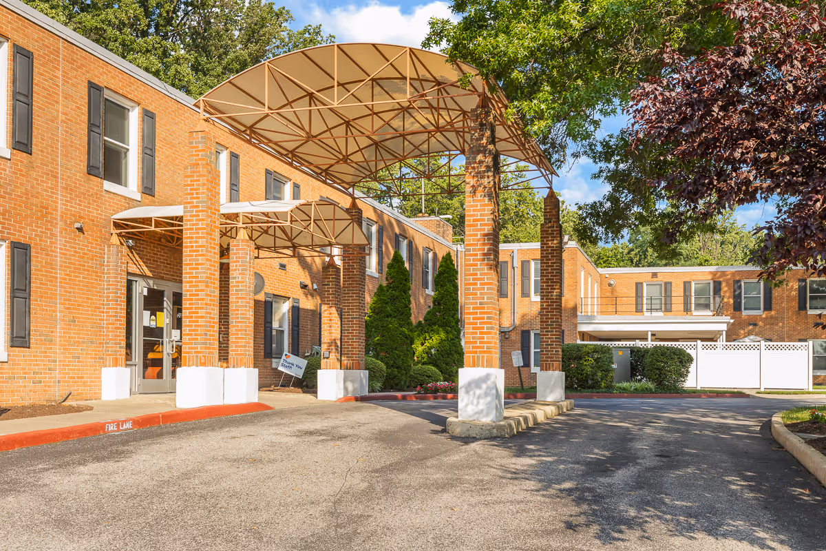 Brick senior living facility front entrance with a covered porte-cochère, driveway, and surrounding landscaping.