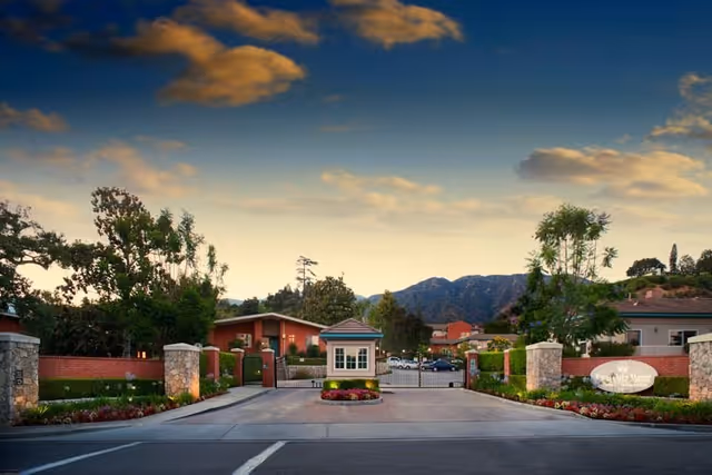 Gated entrance to a senior living community with a guard booth, pillars, and manicured landscaping.