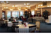 Spacious retirement community dining room with multiple round tables and chairs, sofas, cabinets, and chandeliers.