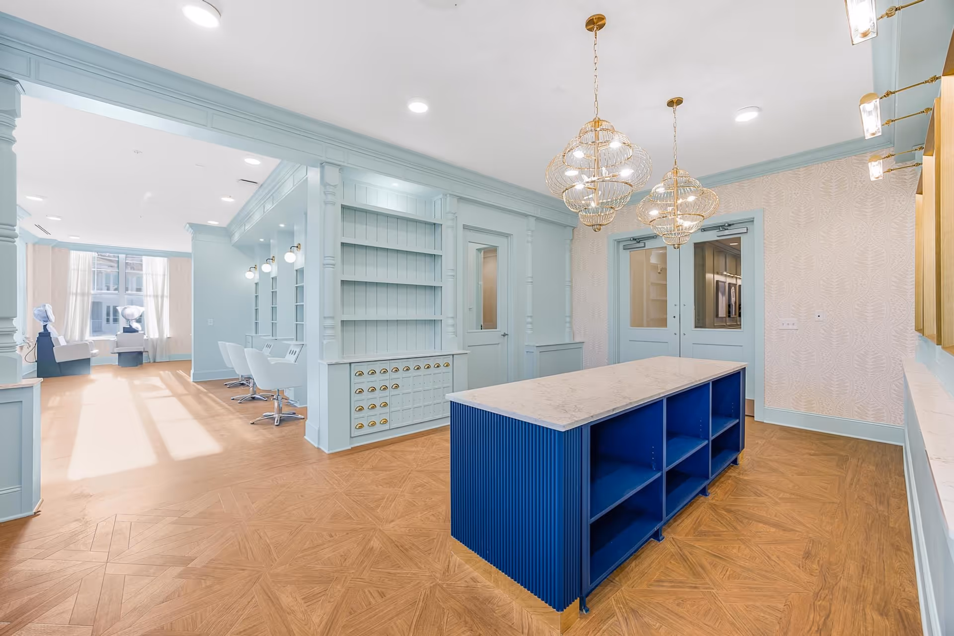 Bright pastel-blue interior salon/common room with a central blue island, pendant lights, and styling chairs and hair stations.
