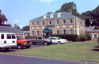 Brick two-story assisted living facility with a parking lot and green lawn in foreground.