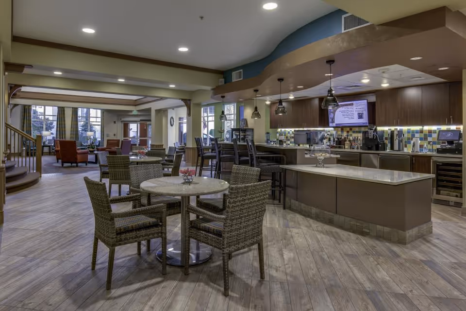 Open dining and café area with round tables and wicker chairs facing a serving counter and lounge seating in the background.