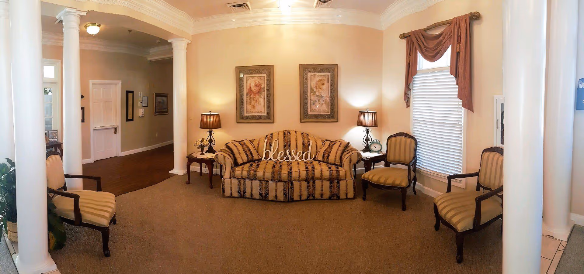 A cozy formal living room with a striped sofa, four armchairs, side tables with lamps, framed art, and white columns.