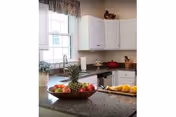 Bright kitchen with white cabinets, a granite island holding a bowl of fruit and lemons, and a window above the sink.