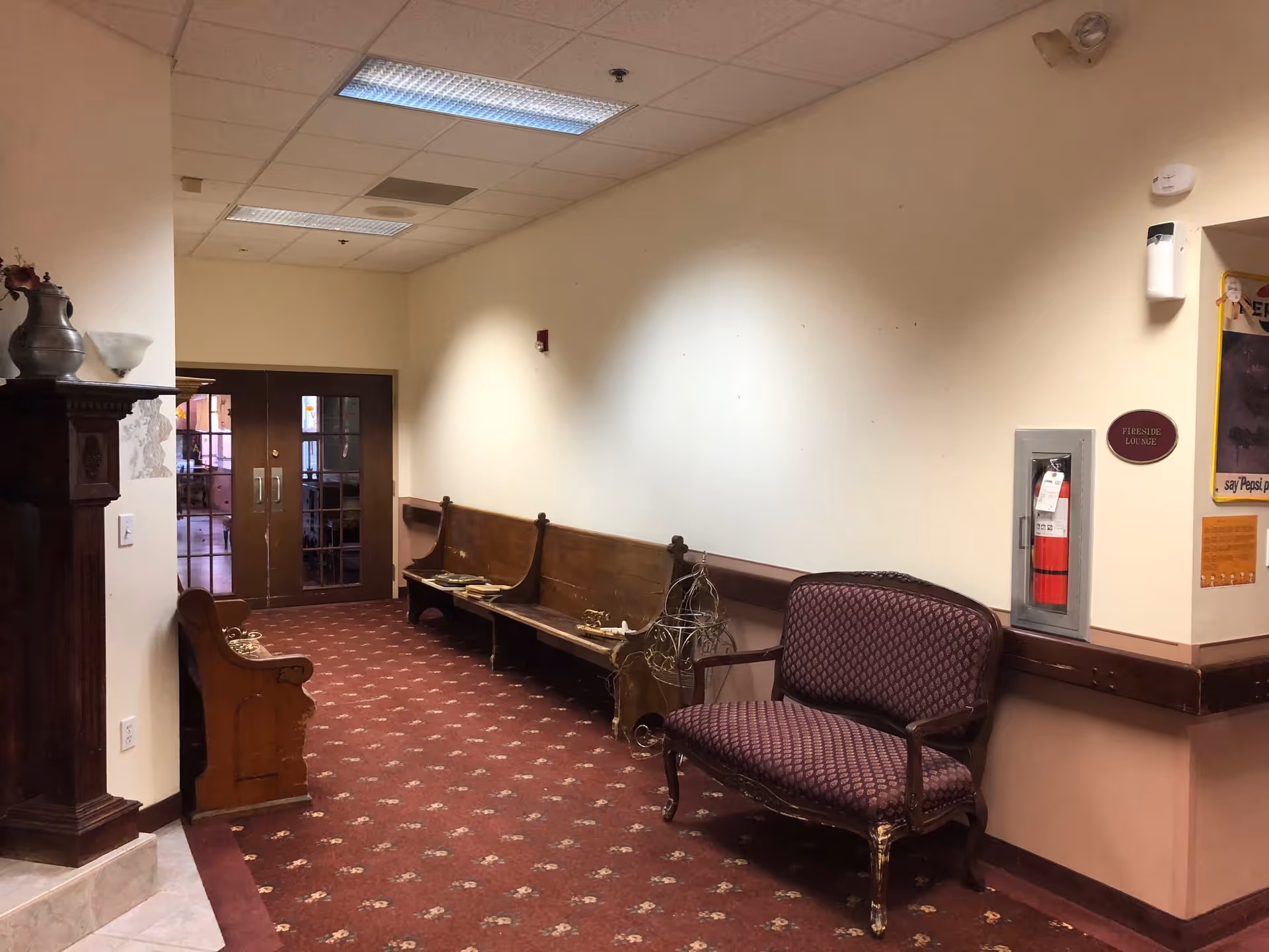 Interior hallway with carpeted floor, wooden bench seating along the wall, an upholstered loveseat, and double doors at the far end.