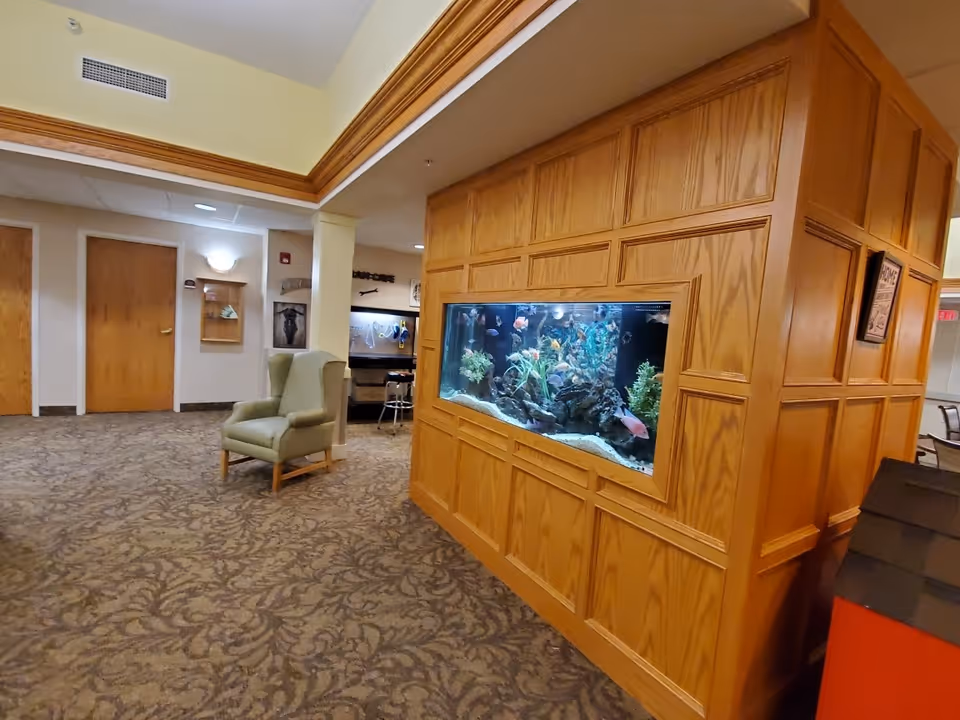 Interior common area with a large built-in aquarium set in a wood-paneled wall, an upholstered armchair, and hallway doors.