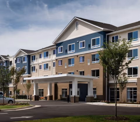 Multi-story senior living facility exterior with blue and tan siding and a covered entrance.