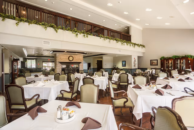 Large dining room with neatly set tables and chairs, a fireplace, and a balcony mezzanine.
