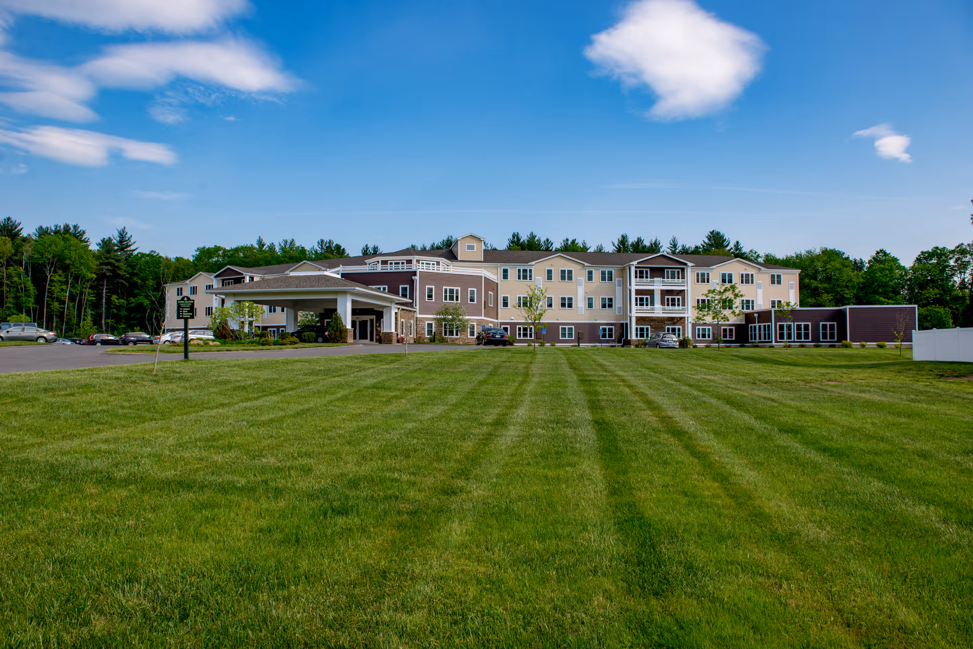 Front view of a three-story assisted living building with a large green lawn and covered entrance.