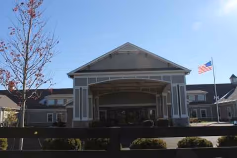 Front view of a senior living center with a covered entrance and flag under blue sky.
