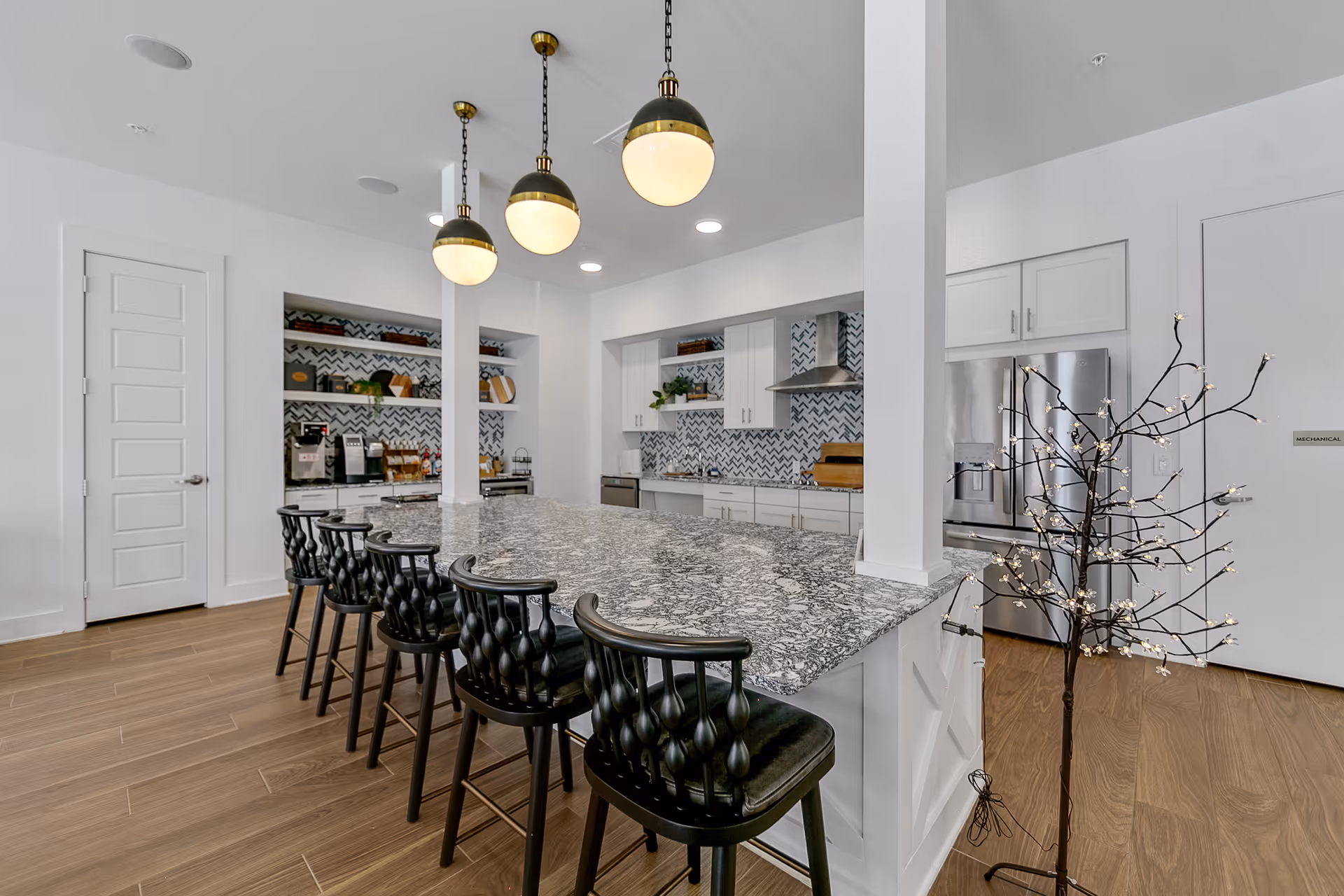 Modern communal kitchen with a large marble island, six black barstools, pendant lights, and stainless steel appliances.