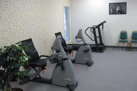 Interior fitness room with stationary bikes, a treadmill, plants, and chairs.